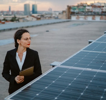 A business woman looking out to a city landscape on a rooftop with solar panels
